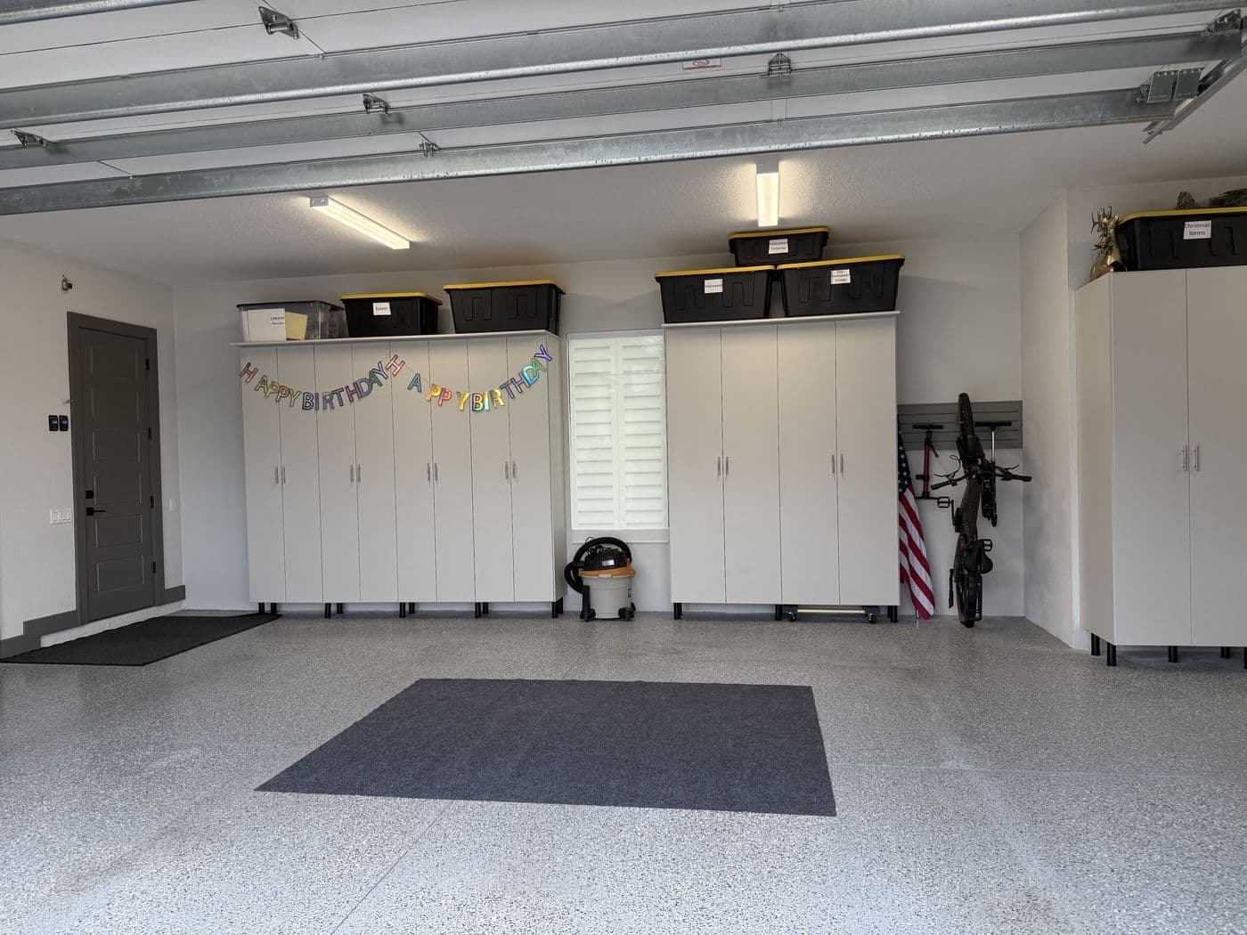 After, the same garage with closed white cabinets along the wall, bins stored on top and a clear floor.